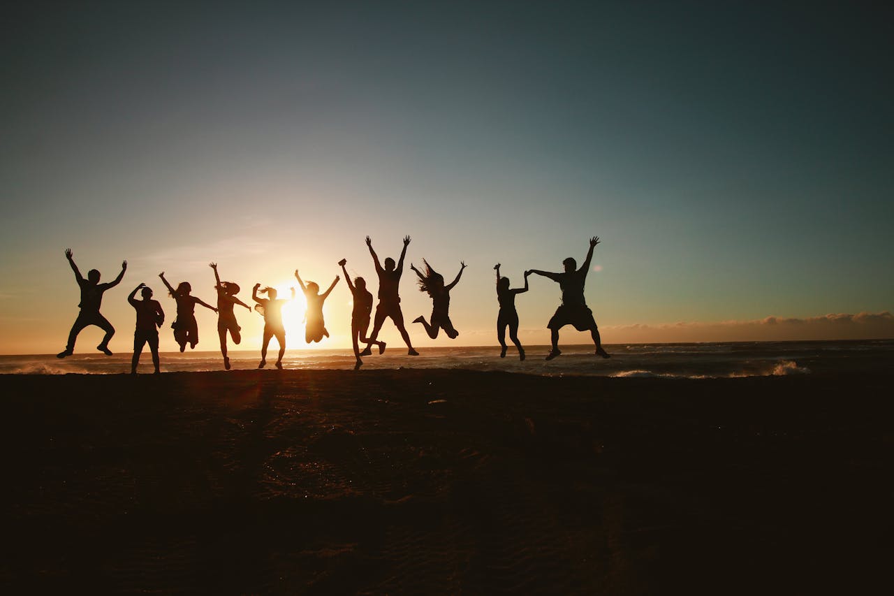 services-01 Silhouette of a group of friends jumping on a beach at sunset, expressing joy and freedom.